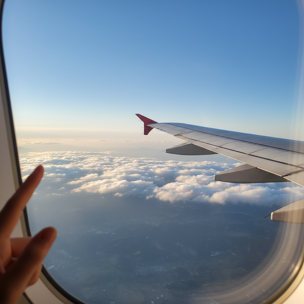 비행기 창밖으로 보이는 구름과 푸른 하늘, 날개 끝이 살짝 보이는 장면